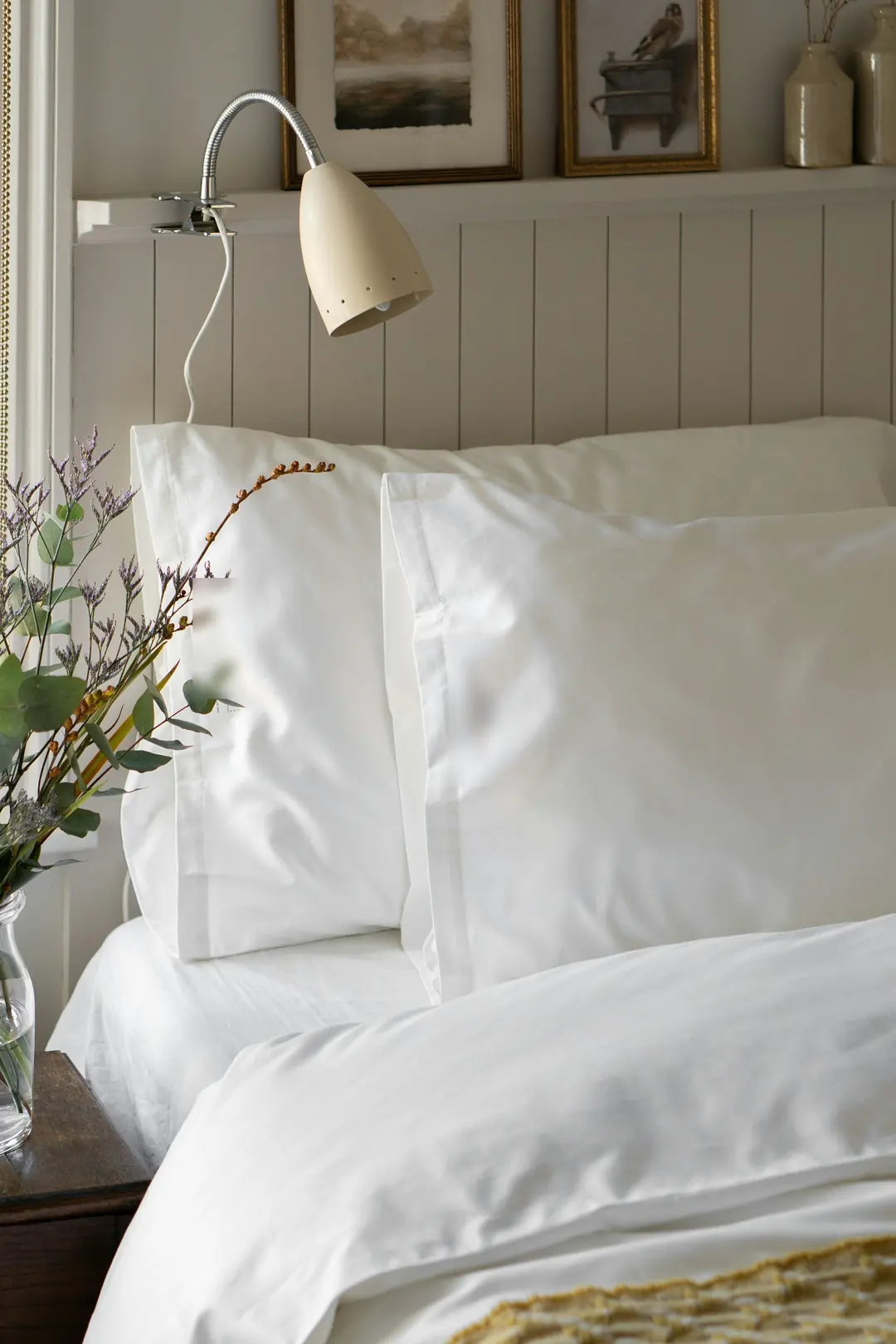 Bed made up in crisp white cotton sheets and pillowcases with a hemmed border, a reading lamp above