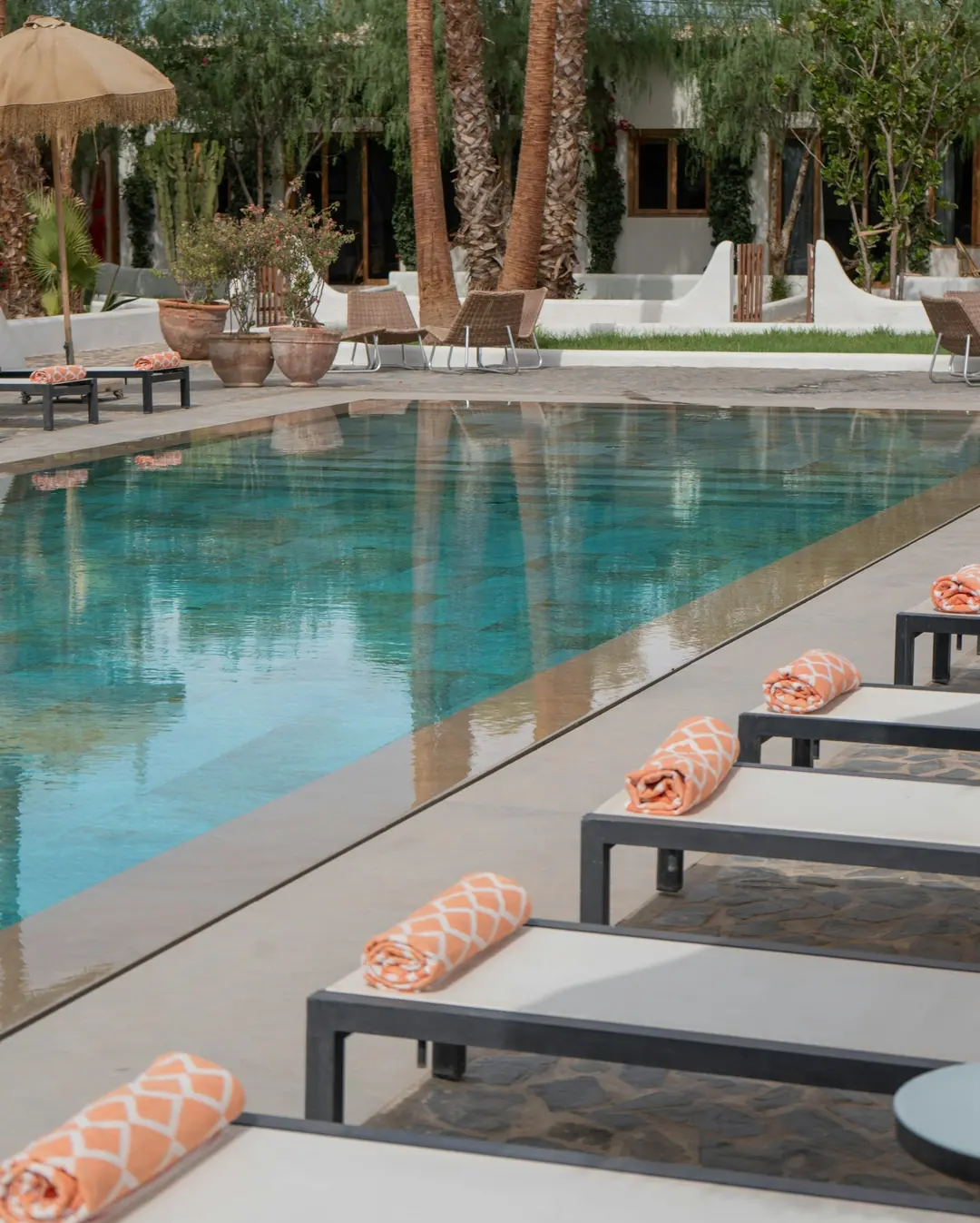 Rolled orange patterned pool towels on loungers along a resort pool with palms and whitewashed walls