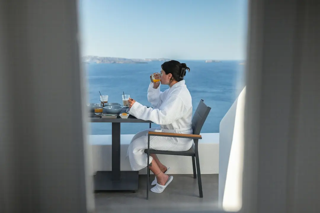 Guest in a waffle bathrobe and white slippers having breakfast on a terrace above the sea