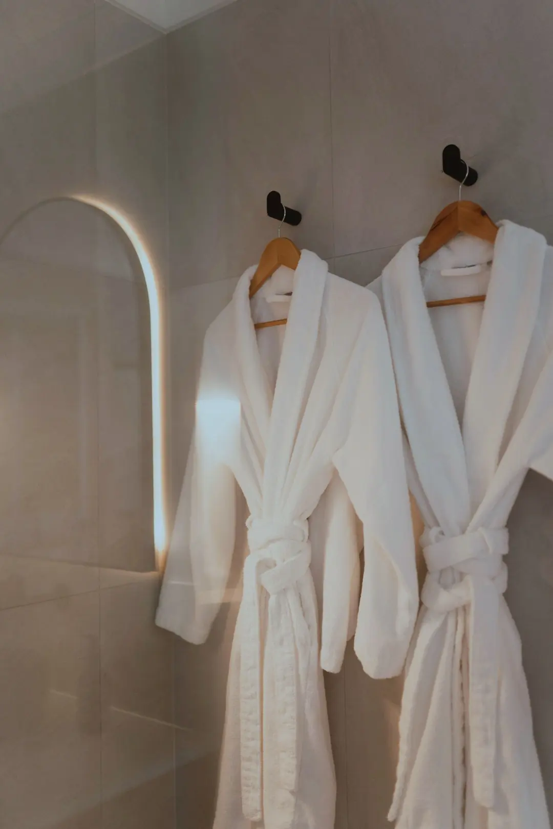 Two white bathrobes hanging on hooks in an arched bathroom niche