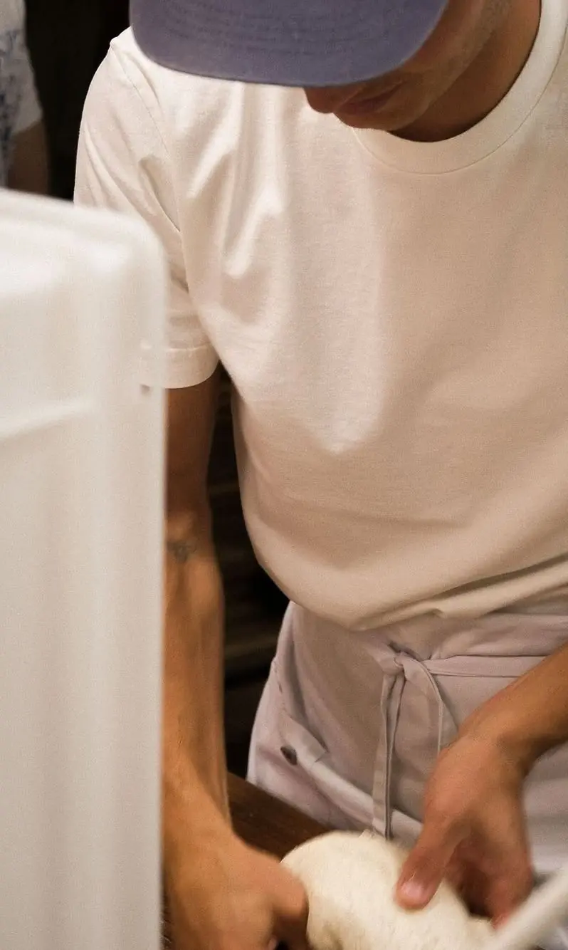 Baker in a white T-shirt and white apron shaping dough at the counter