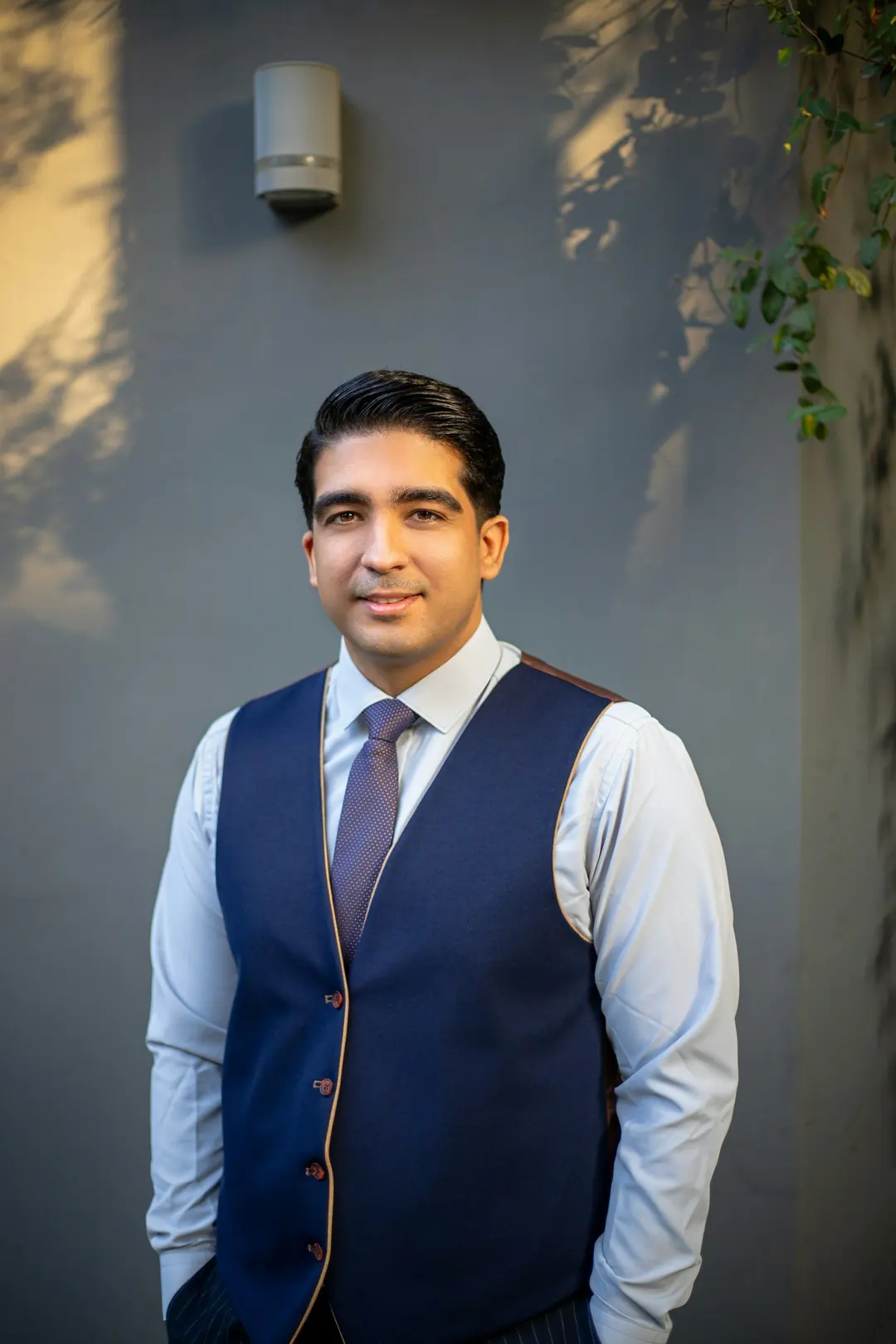 Front-of-house team member in a navy waistcoat with contrast piping, shirt and tie